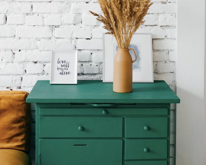 green cabinet with drawers and a vase full of dried bentgras and a framed text saying 'love will keep us alive' on top of it